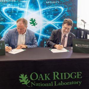 Matt Miles and Stephen Streiffer sign documents at a table during an MOU signing ceremony at the NOW Conference.