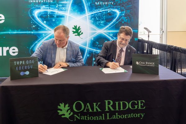 Matt Miles and Stephen Streiffer sign documents at a table during an MOU signing ceremony at the NOW Conference.