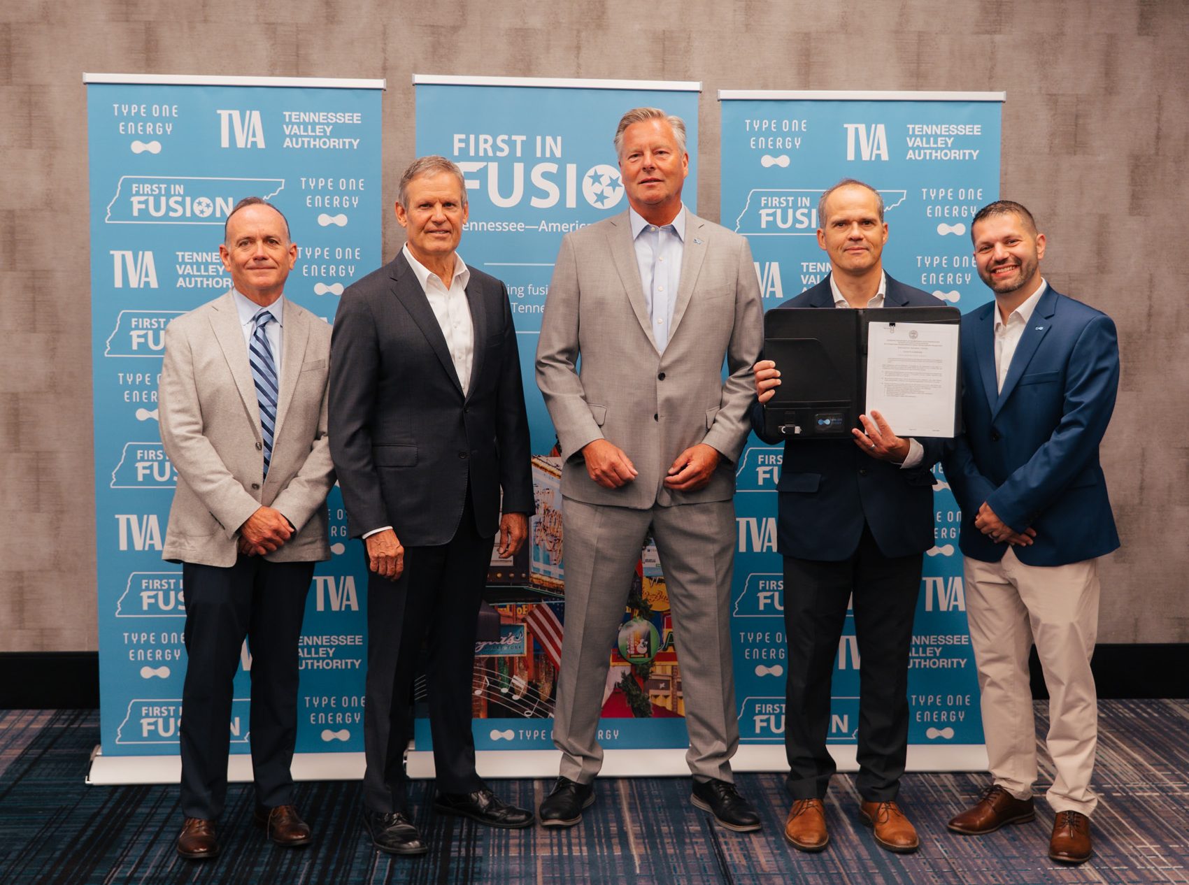 Tennessee Governor Bill Lee stands inside a hotel conference room with a group of officials from Type One Energy and TVA in front of a sign that reads "First in Fusion."